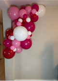 Balloon arch with pink, red, and white balloons against a plain wall.
