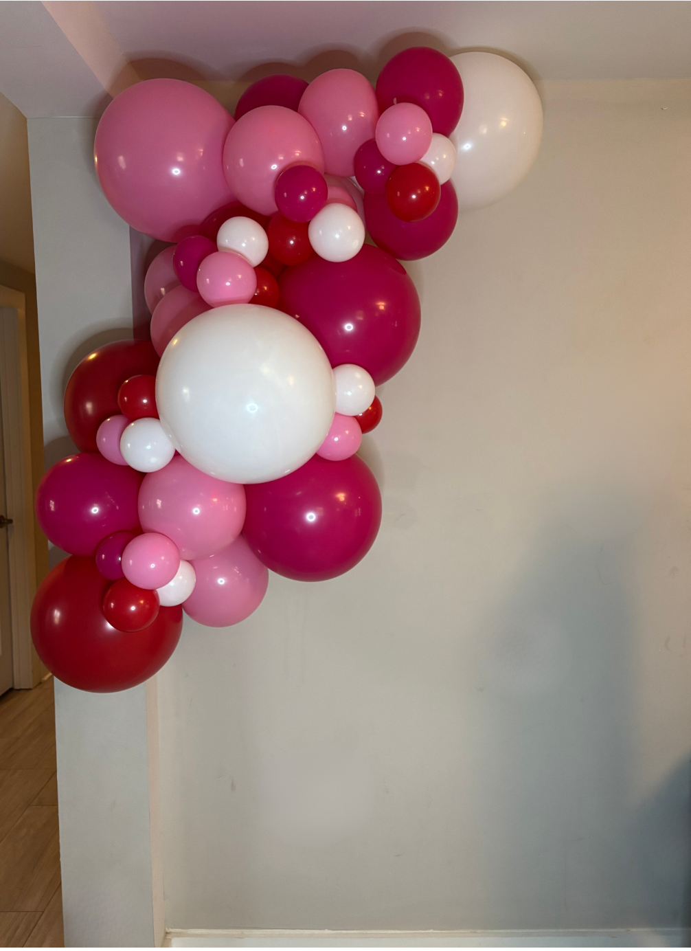 Balloon arch with pink, red, and white balloons against a plain wall.